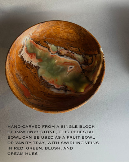 Translucent onyx pedestal bowl held against natural light showing glowing green, amber, and earthy brown stone layers
