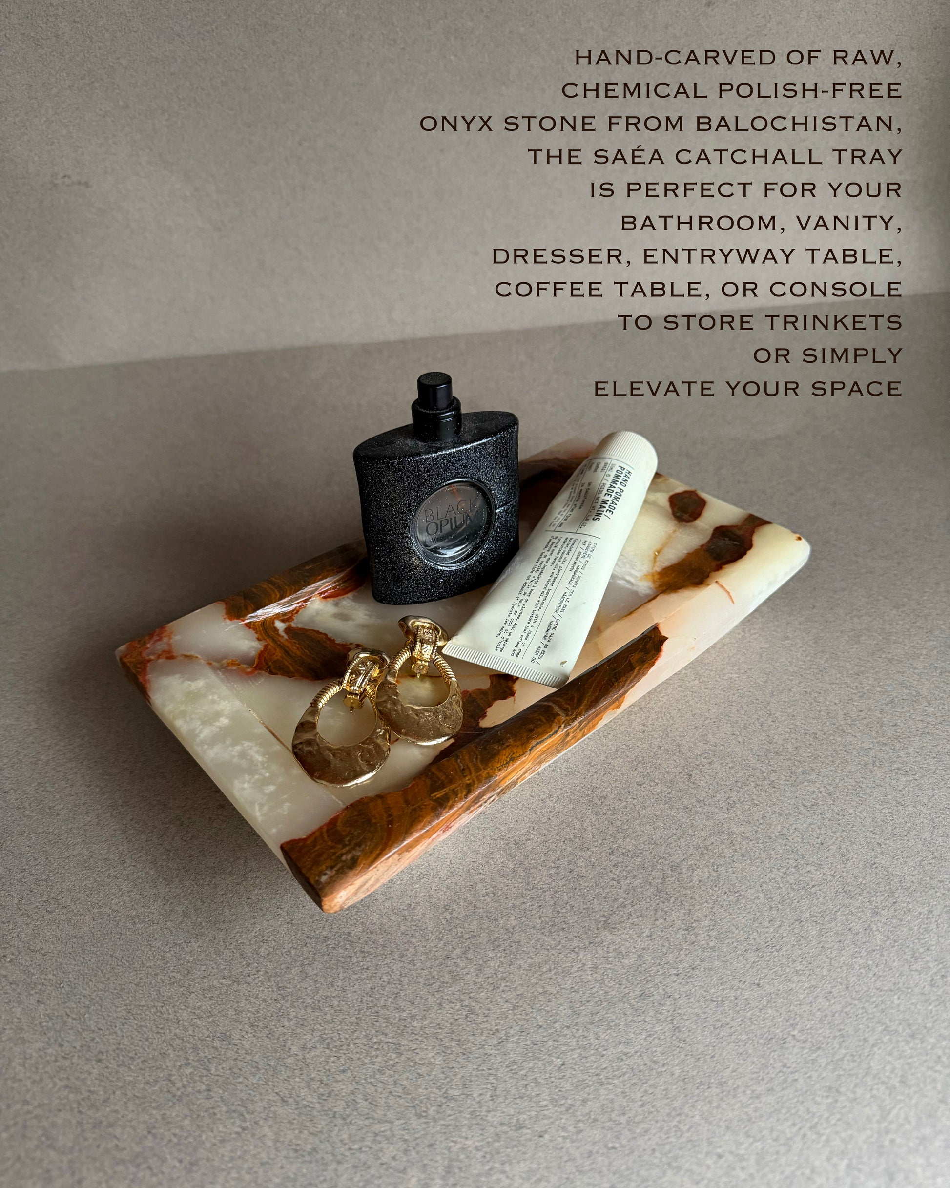 Onyx catchall tray with a black bottle, keys, and tube of cream on a gray surface.