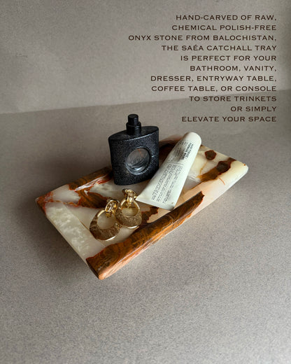 Onyx catchall tray with a black bottle, keys, and tube of cream on a gray surface.