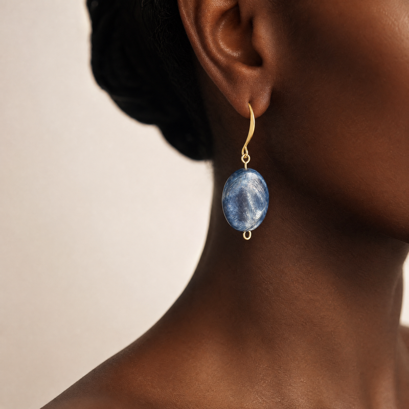 Close-up of an ear wearing a blue kyanite spherical earring with gold accents against a neutral background