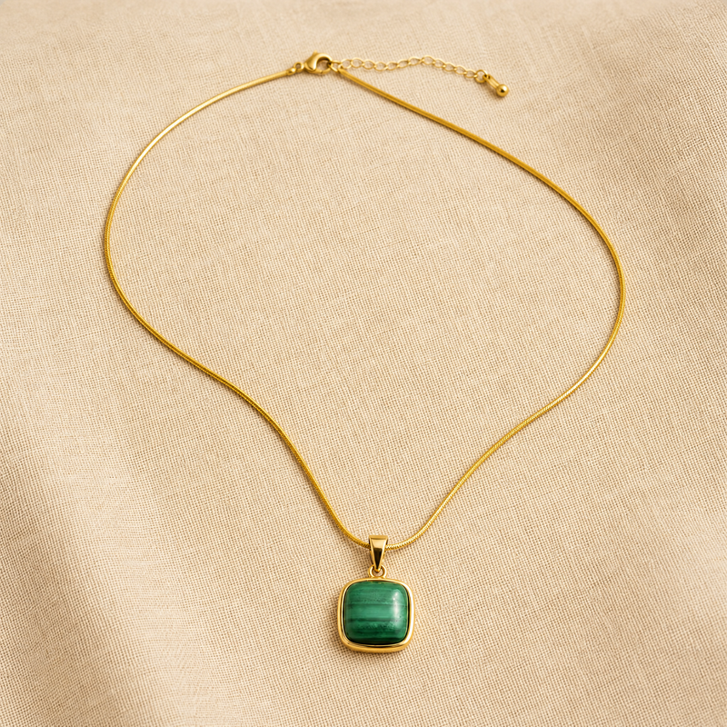 Gold snake chain necklace with a green malachite stone pendant on a beige fabric background