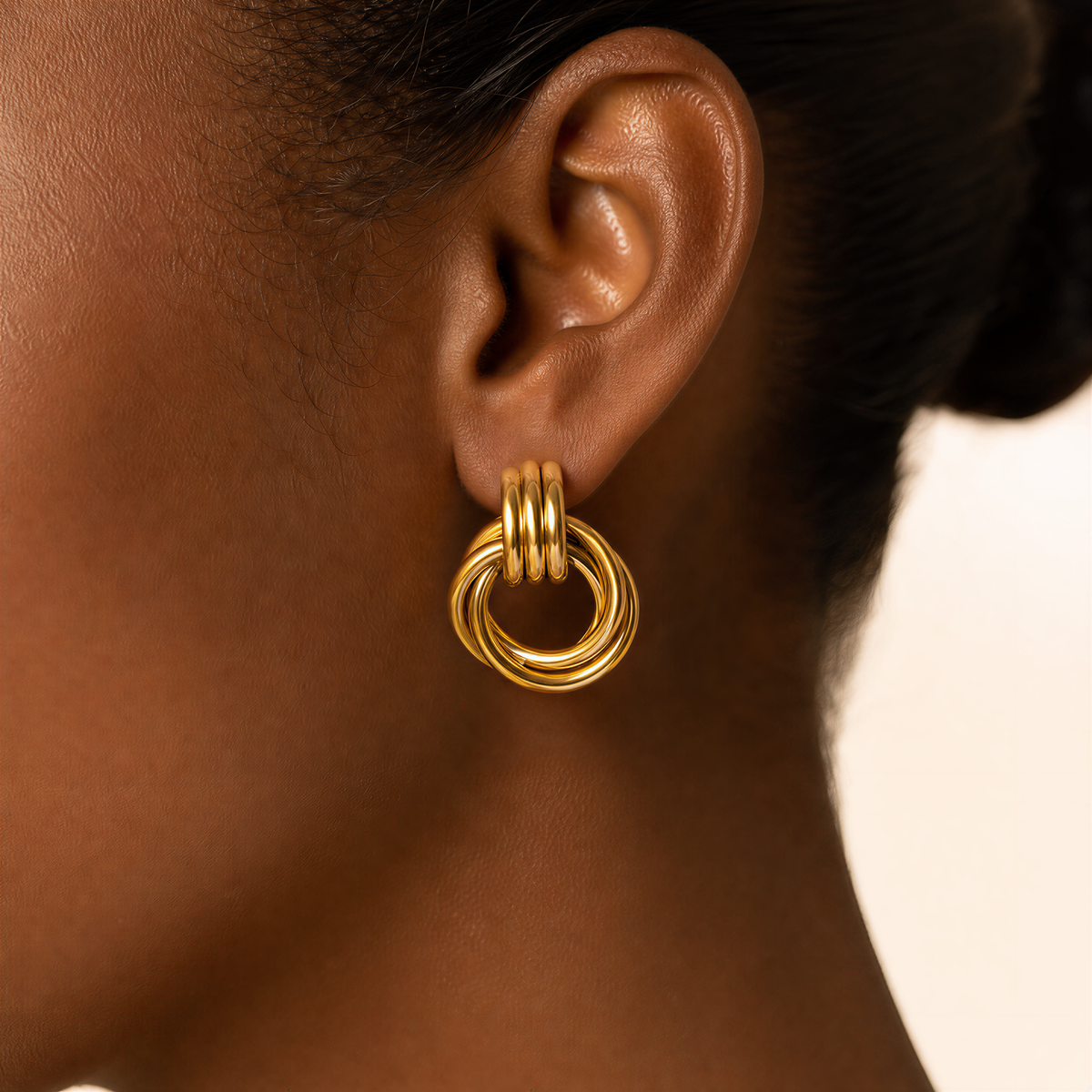 Model wearing a gold interlocking knot earring, ribbed triple band linking into a twisted ring drop, side profile. Heaven Mayhem Dupe
