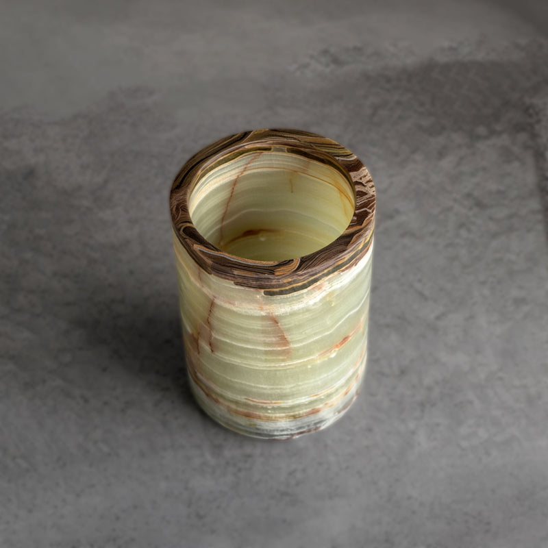 Sage green onyx vessel styled as a bathroom toothbrush holder with bamboo brushes beside soap and ceramic vases
