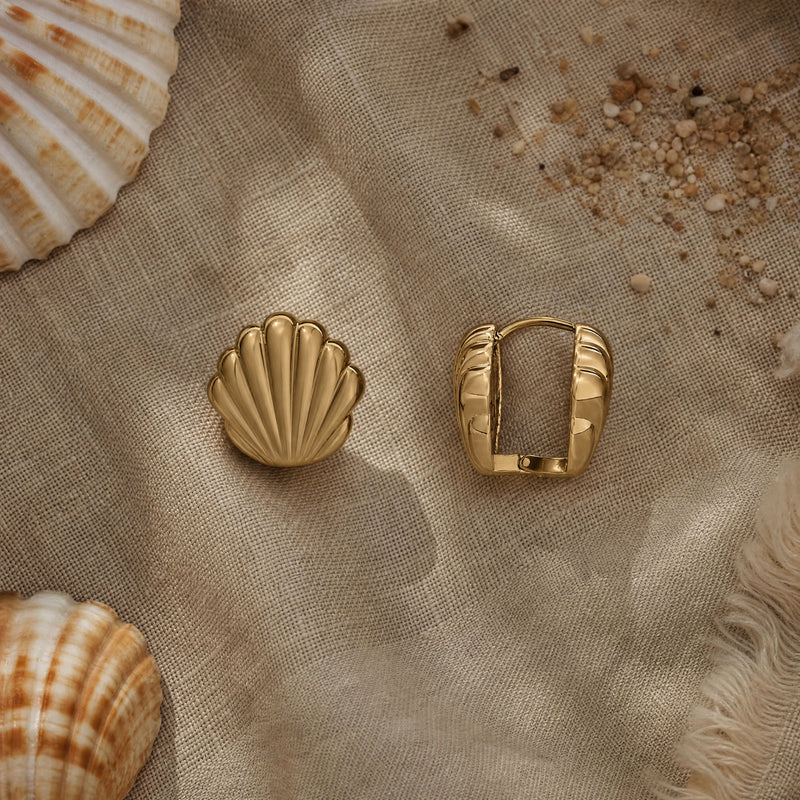 Gold shell and square hoop earrings on a textured beige fabric background with seashells.
