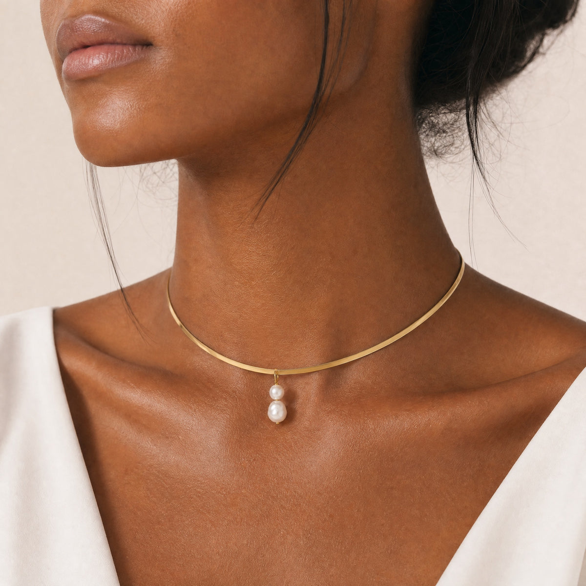 Gold necklace with a freshwater pearl pendant on a model against a neutral background