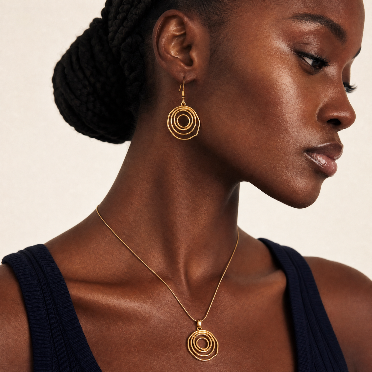 Woman wearing gold circular spiral gold sculptural earrings and necklace against a neutral background