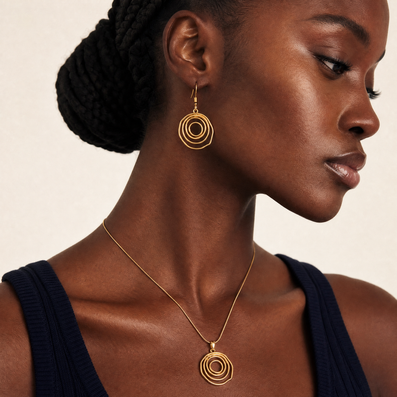 Woman wearing gold circular spiral gold sculptural earrings and necklace against a neutral background