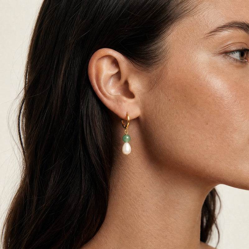 Close-up of a woman wearing huggie hoop tiny minimalist earrings with a blue gemstone and neutral background