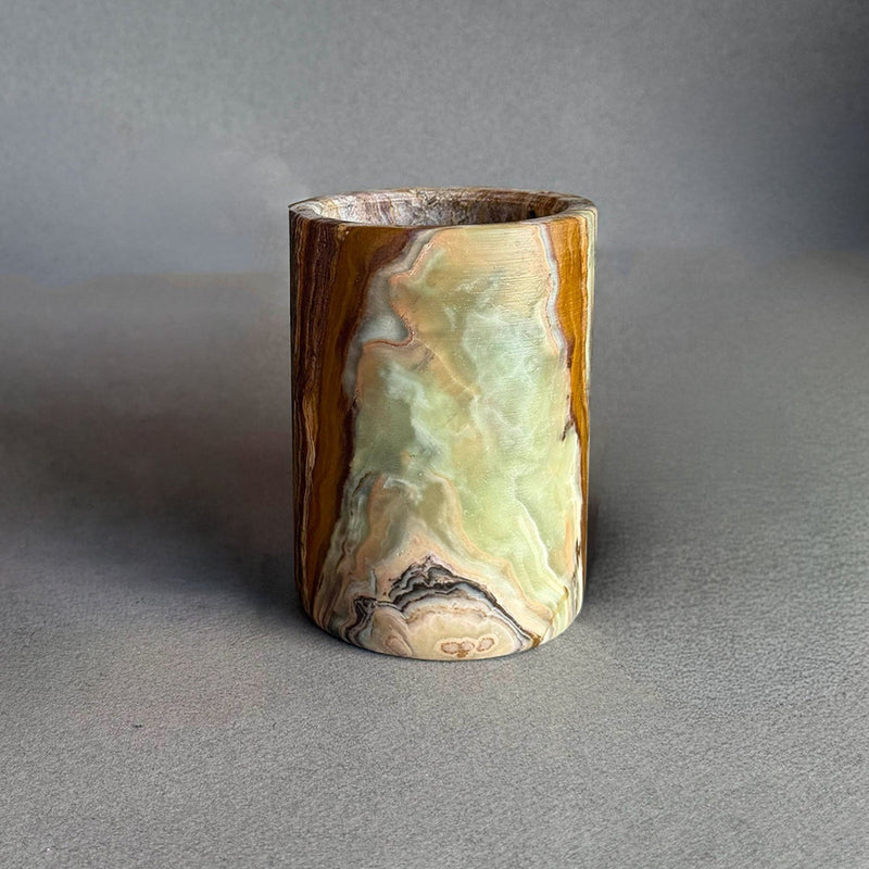 Marbleized cylindrical green onyx jar on a gray surface with a neutral background