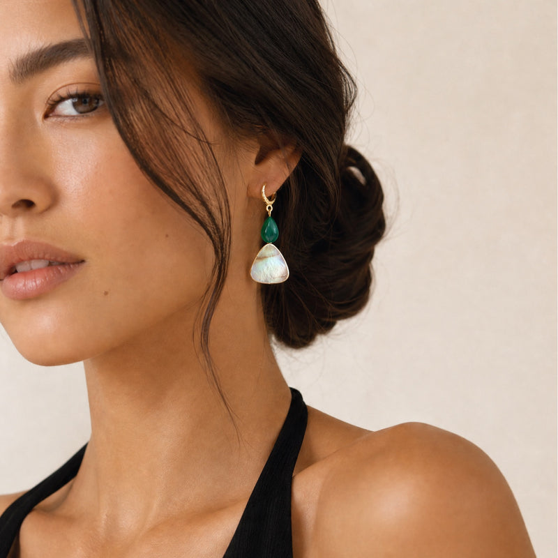 Woman wearing a black top and green malachite and white mother of pearl earrings against a beige background