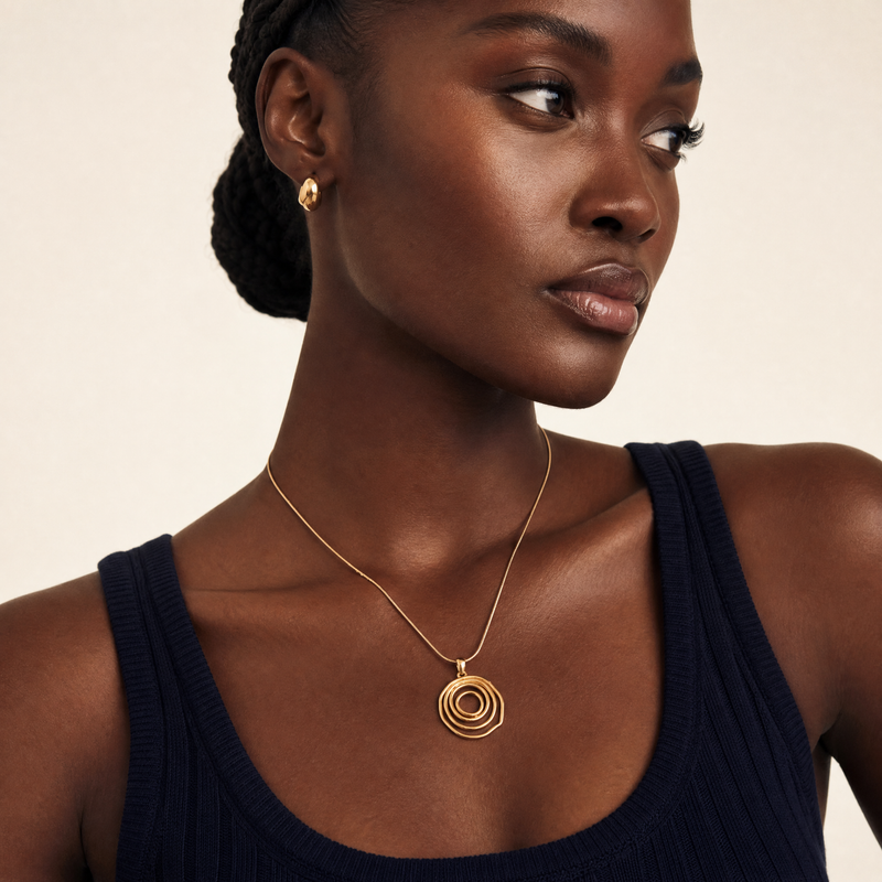Woman wearing a gold spiral statement necklace and earrings on a beige background with a snake chain