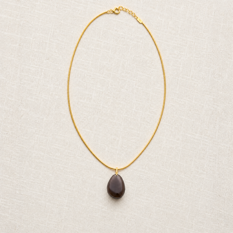 Gold snake chain necklace with a dark brown teardrop obsidian pendant on a light gray background