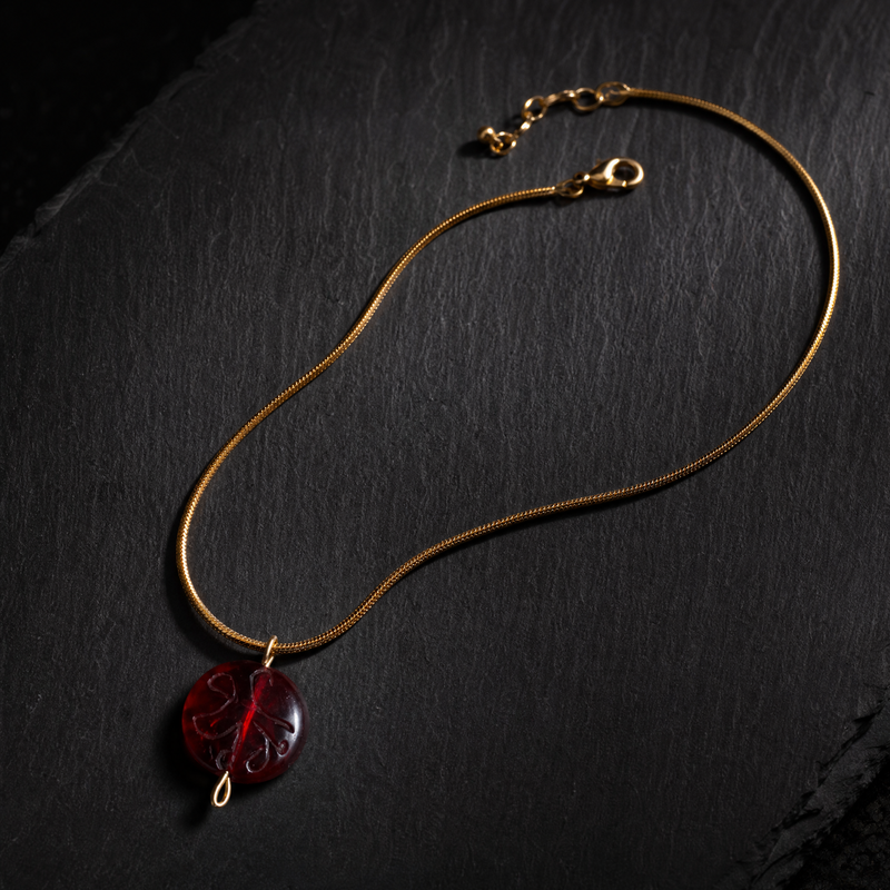 Gold necklace with a red pendant on a dark surface