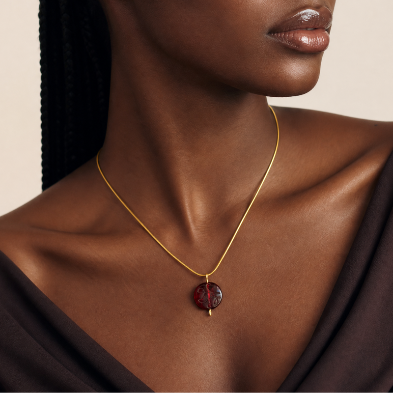 Woman wearing a gold necklace with a red garnet glass pendant against a neutral background