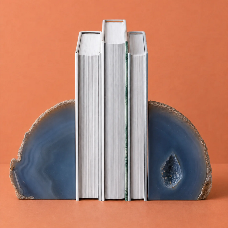 Three white books standing upright between two blue agate slice bookends on a solid terracotta background.