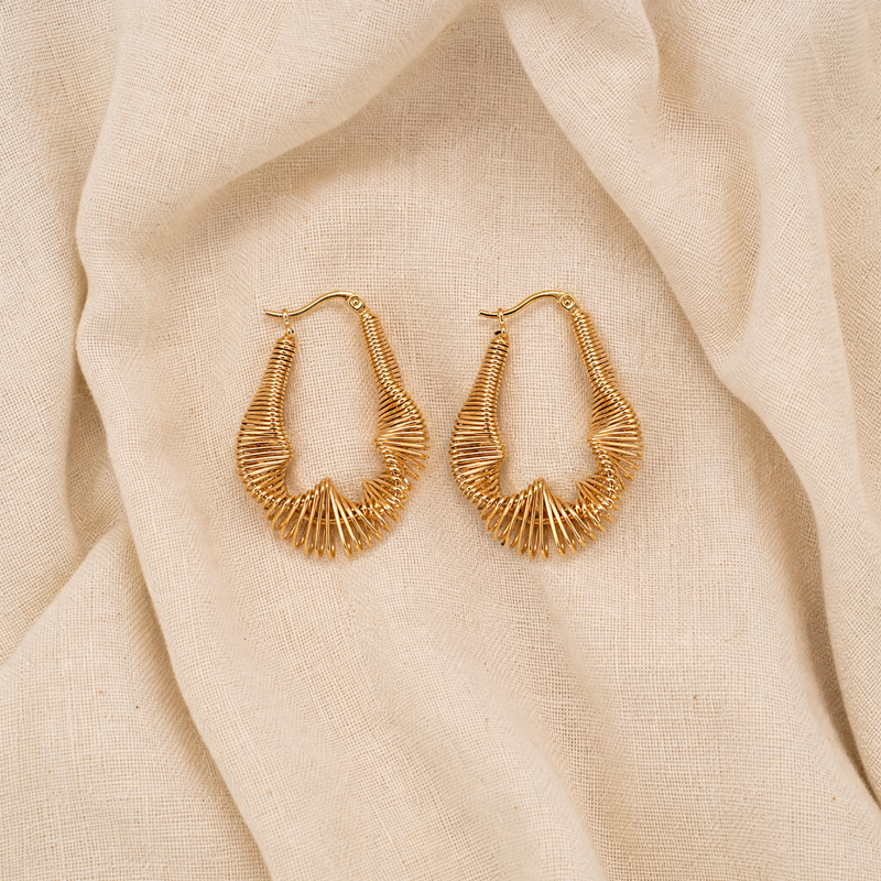 Model wearing Surena Spiral Hoops by SAÉA — 18k gold plated wire earrings with spiral shell form, front-facing portrait view.