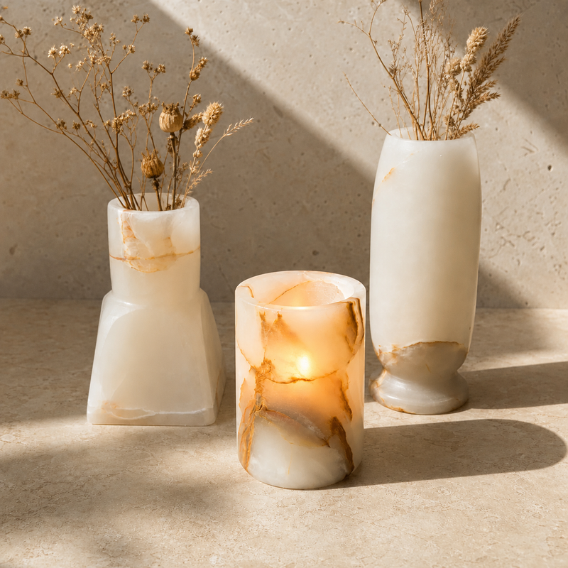Three white onyx stone vases with dried floral arrangements, styled on a beige stone surface with warm sunlight and shadows.