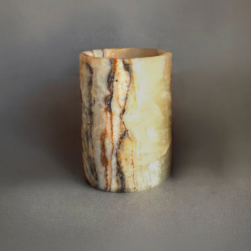 Hand-carved natural yellow onyx vessel with honey, amber, and charcoal veining, cylindrical stone holder on gray background.