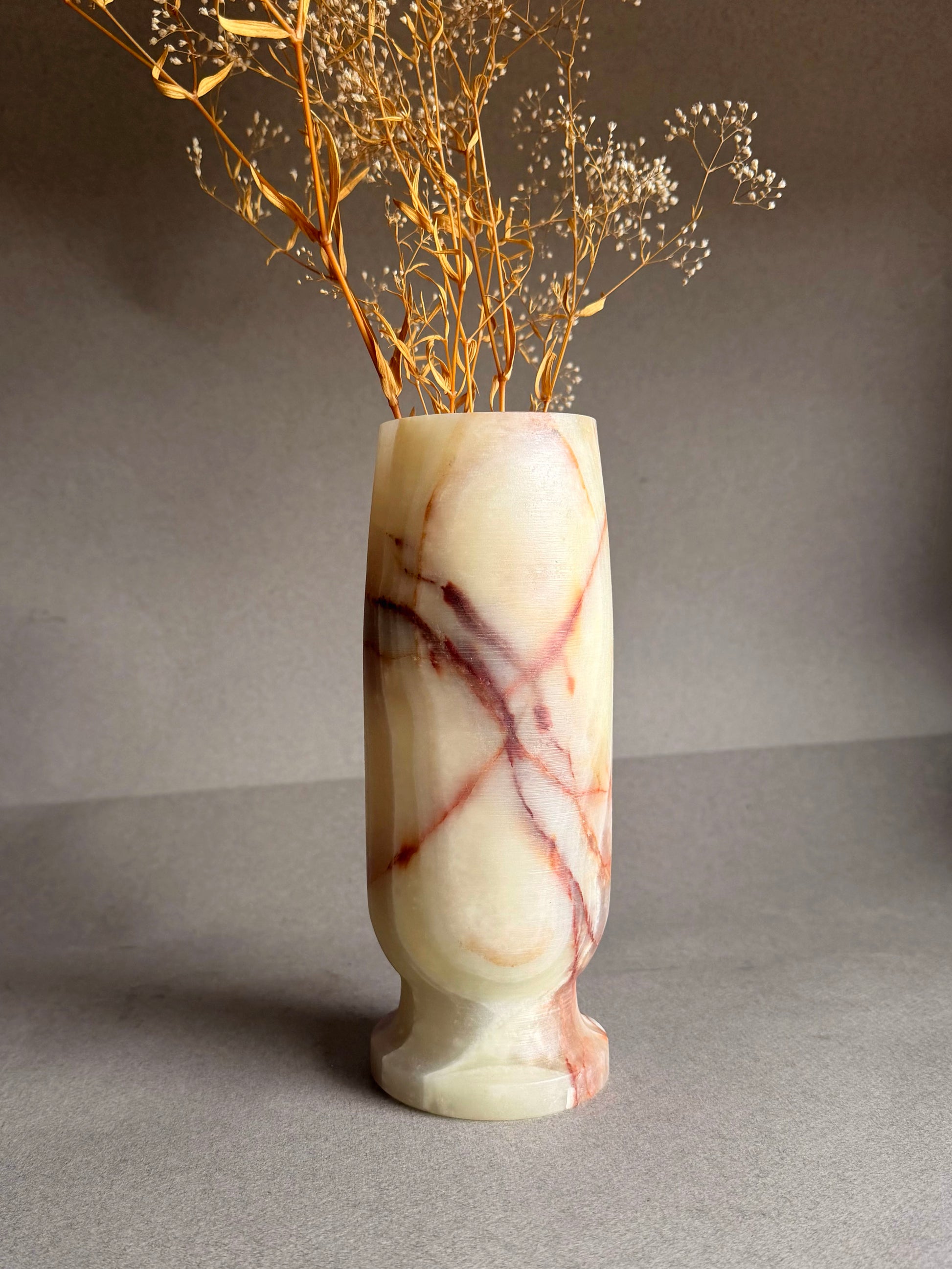 Marble-patterned onyx vase with dried branches on a gray background