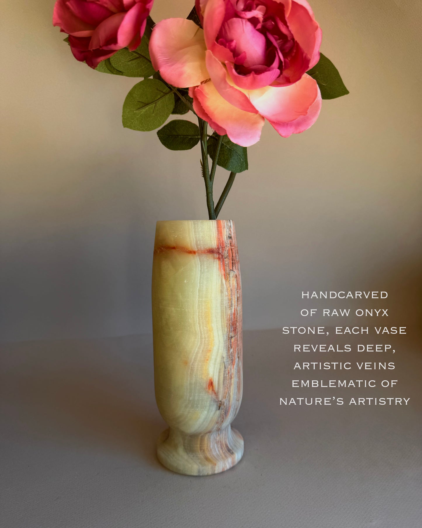 Handcarved onyx stone vase with pink flowers on a neutral background