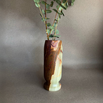 Brown green raw onyx natural stone vase with a natural grain pattern on a gray background