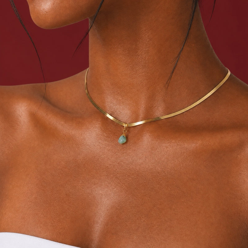 Close-up of a woman wearing a gold snake chain necklace choker 14 inch with a blue stone aquamarine pendant on a beige background