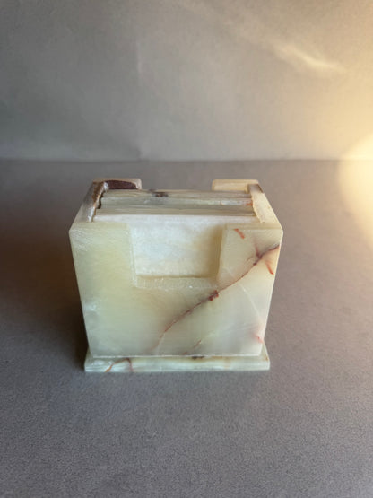 Stone coaster holder in ivory onyx with amber and rust veining, carved square form with matte finish.