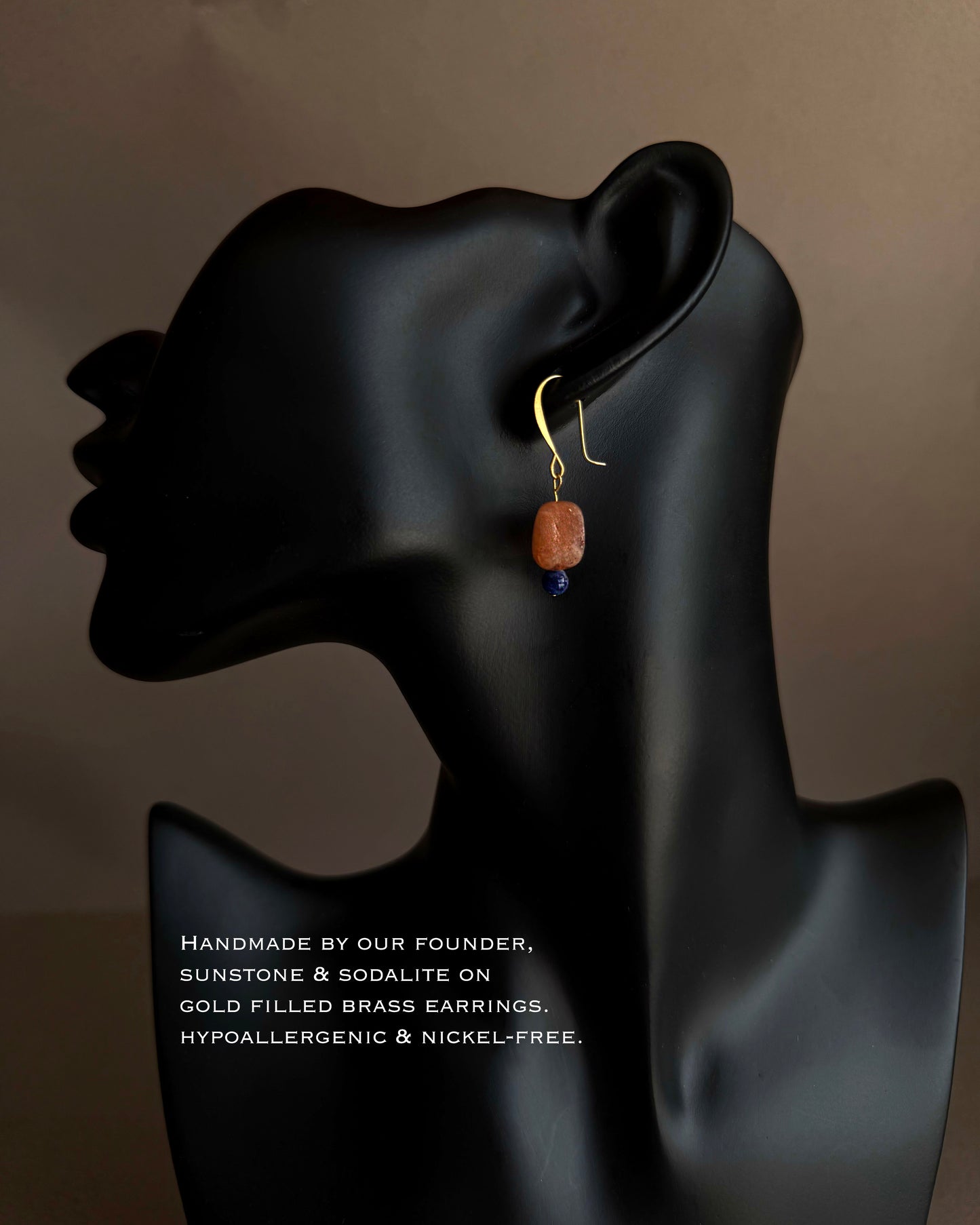 Earring displayed on a black mannequin ear with text about the earring's materials and features. Sunstone and sodalite gemstone earrings with warm peach stone and deep blue accent bead
