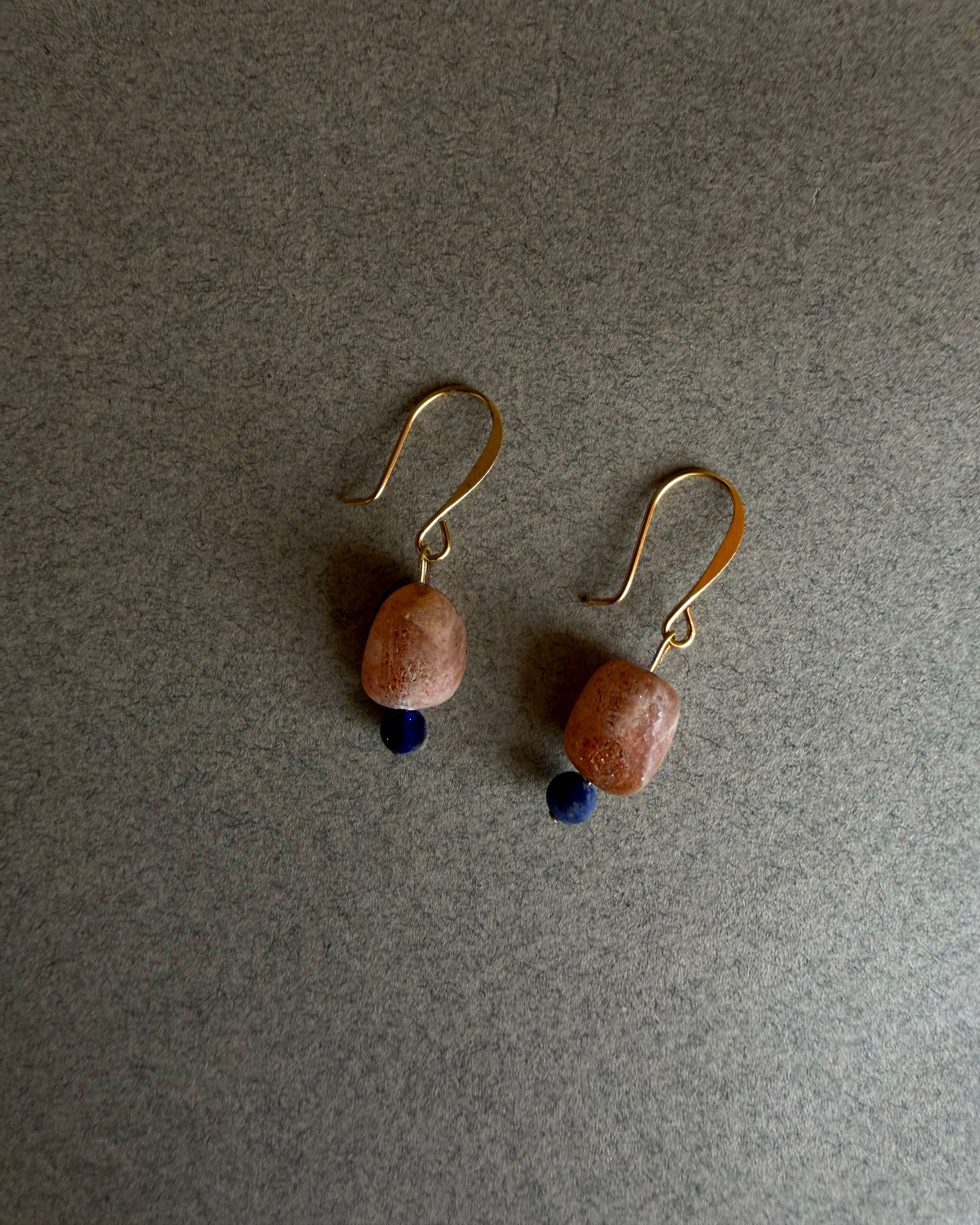 Pair of earrings with brown beads and gold hooks on a gray background Gold filled gemstone earrings with raw sunstone and deep blue sodalite accent
