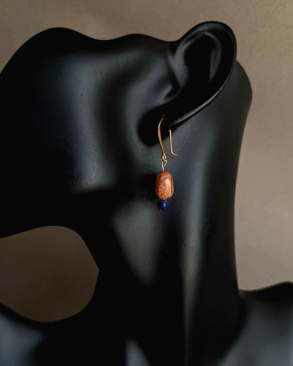 Earring with a brown bead and blue gemstone on a black mannequin ear. Natural sunstone and sodalite earrings worn on black sculptural bust, modern artisan jewelry

