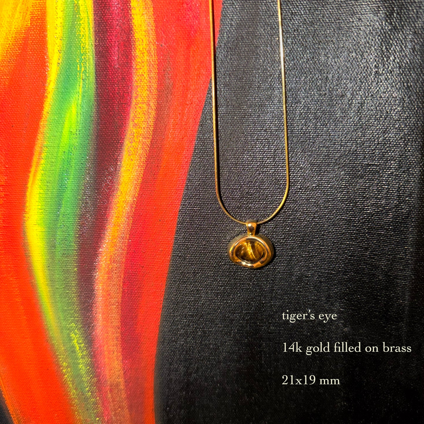 Gold necklace with a tiger's eye pendant on a colorful abstract background