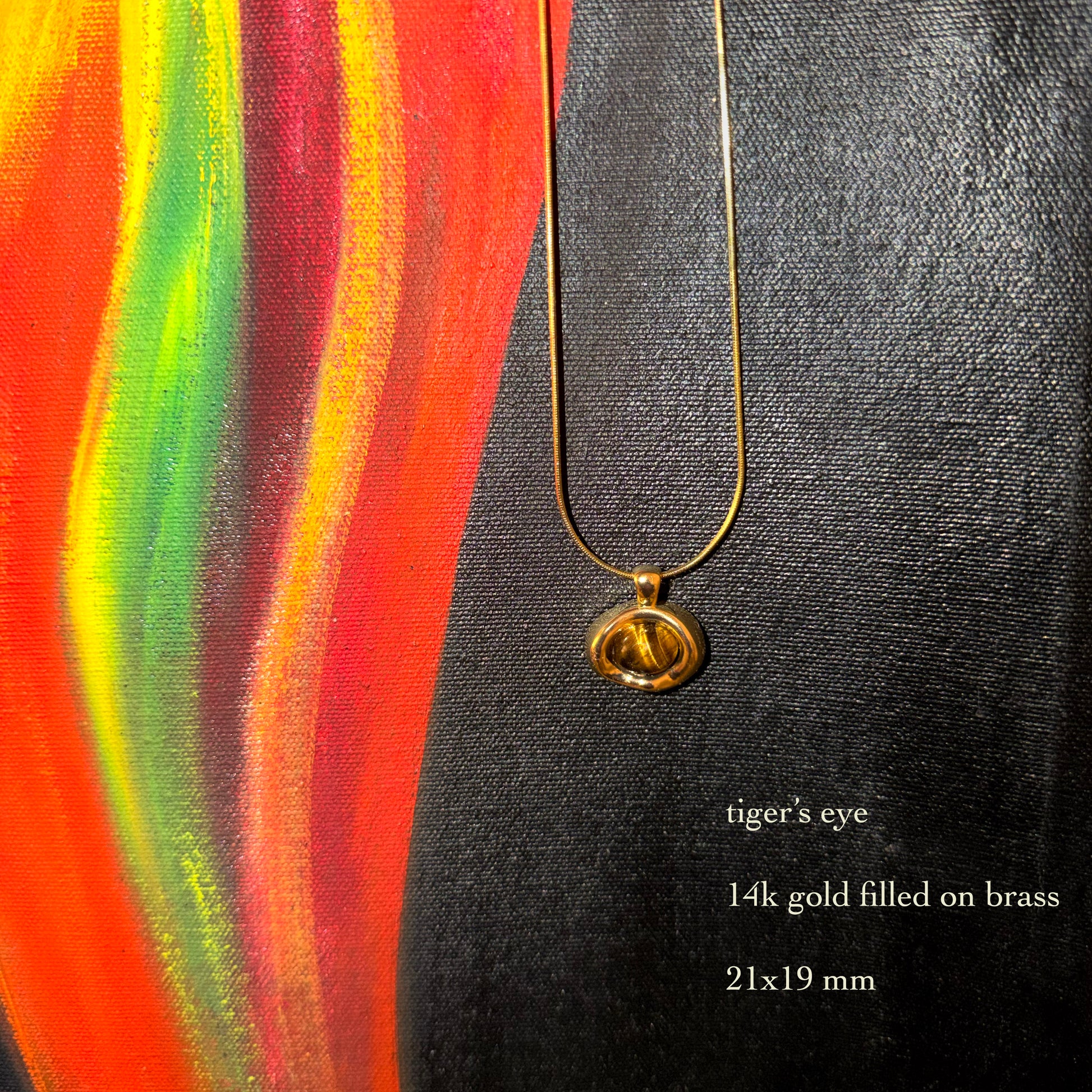 Gold necklace with a tiger's eye pendant on a colorful abstract background