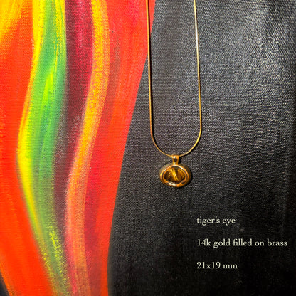 Gold necklace with a tiger's eye pendant on a colorful abstract background