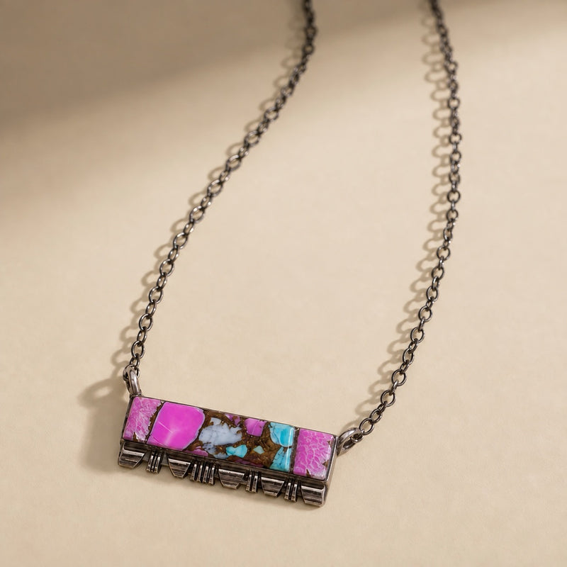 Southwestern pink Mojave turquoise bar necklace in oxidized sterling silver with a hand-stamped base, laid flat on cream