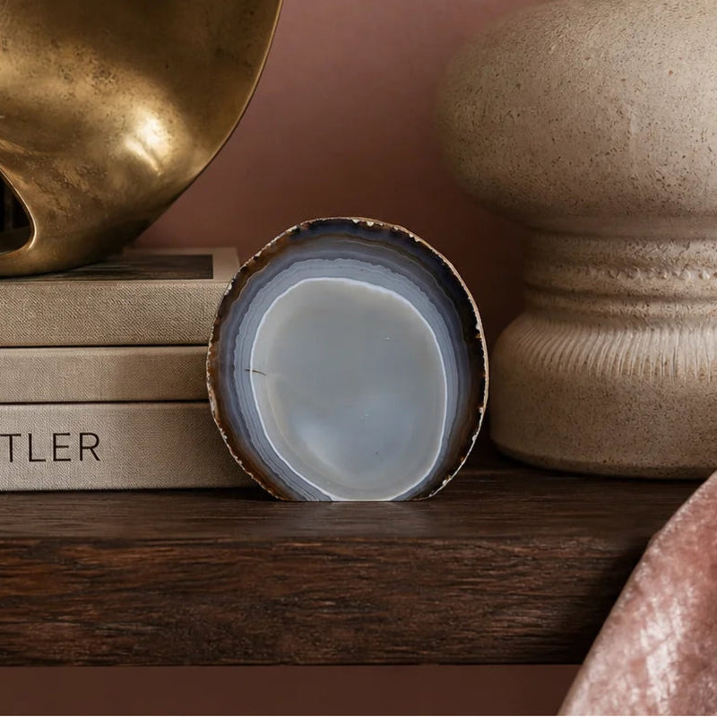 Umber and dove standing agate on a dark shelf with a stone vase and brass sculpture, pink wall