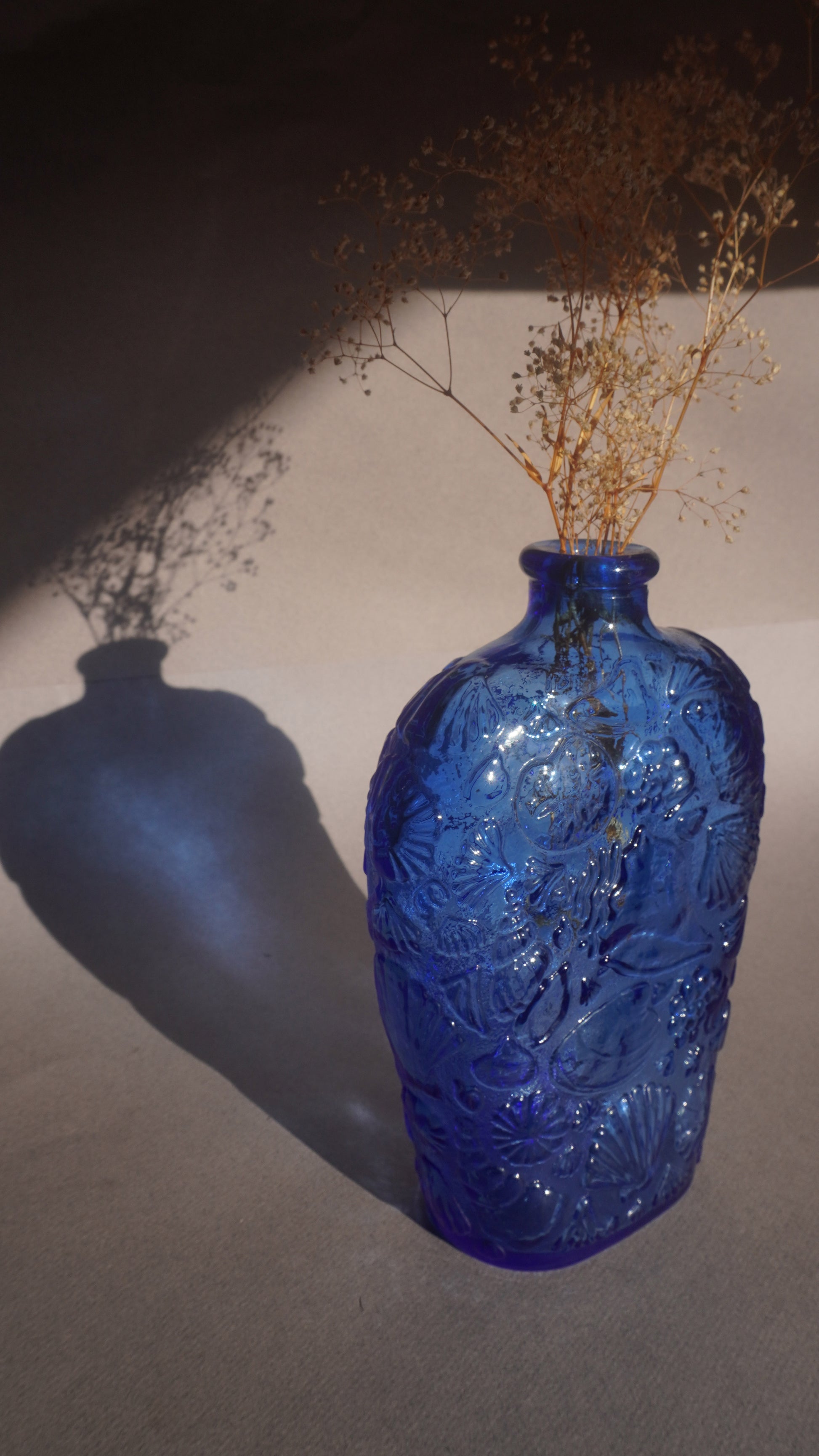 Blue textured vase with dried plants against a neutral background