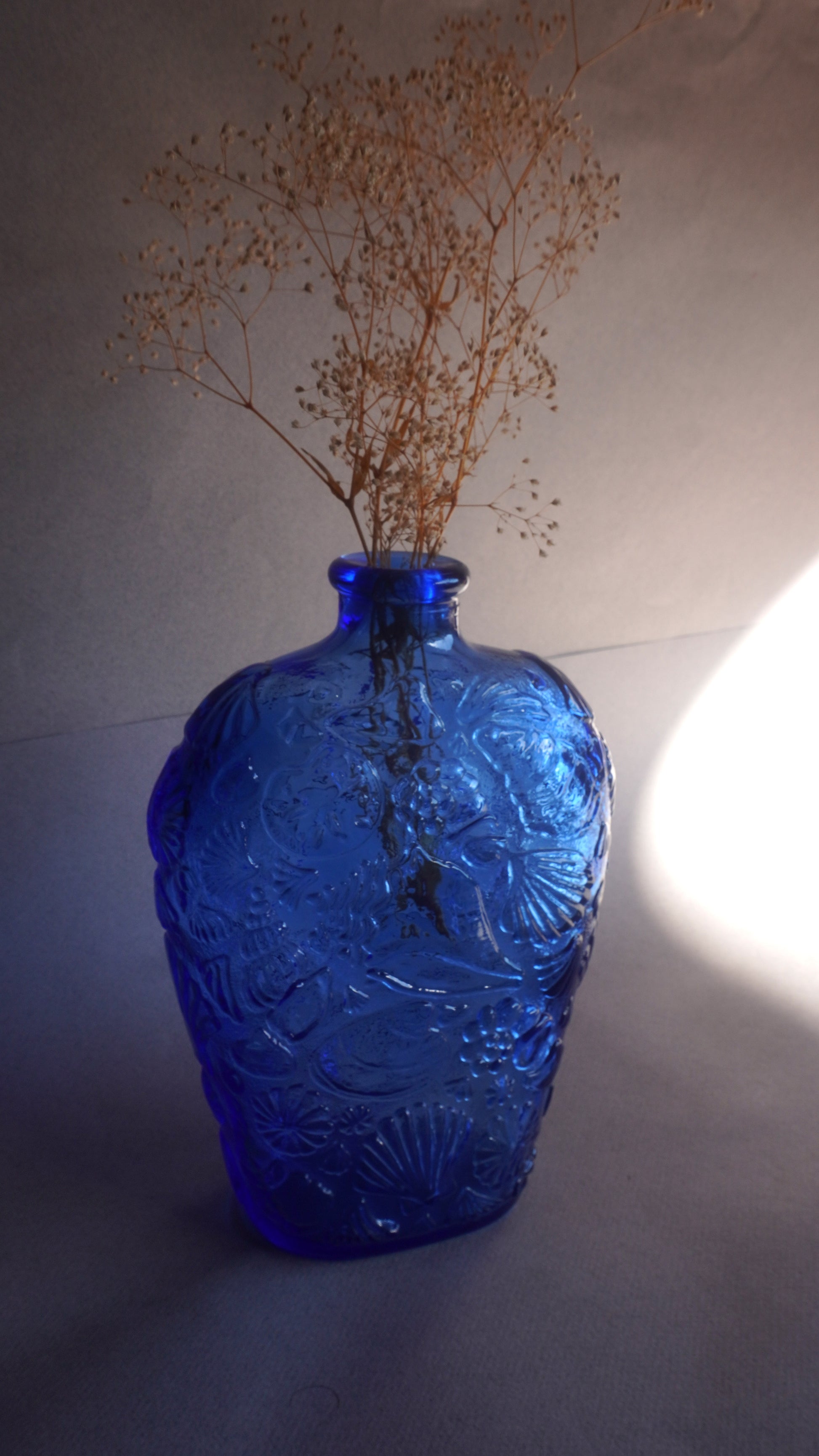 Blue glass vase with intricate patterns and dried plants on a neutral background