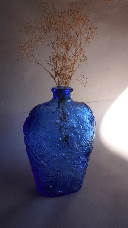 Blue glass vase with intricate patterns and dried plants on a neutral background