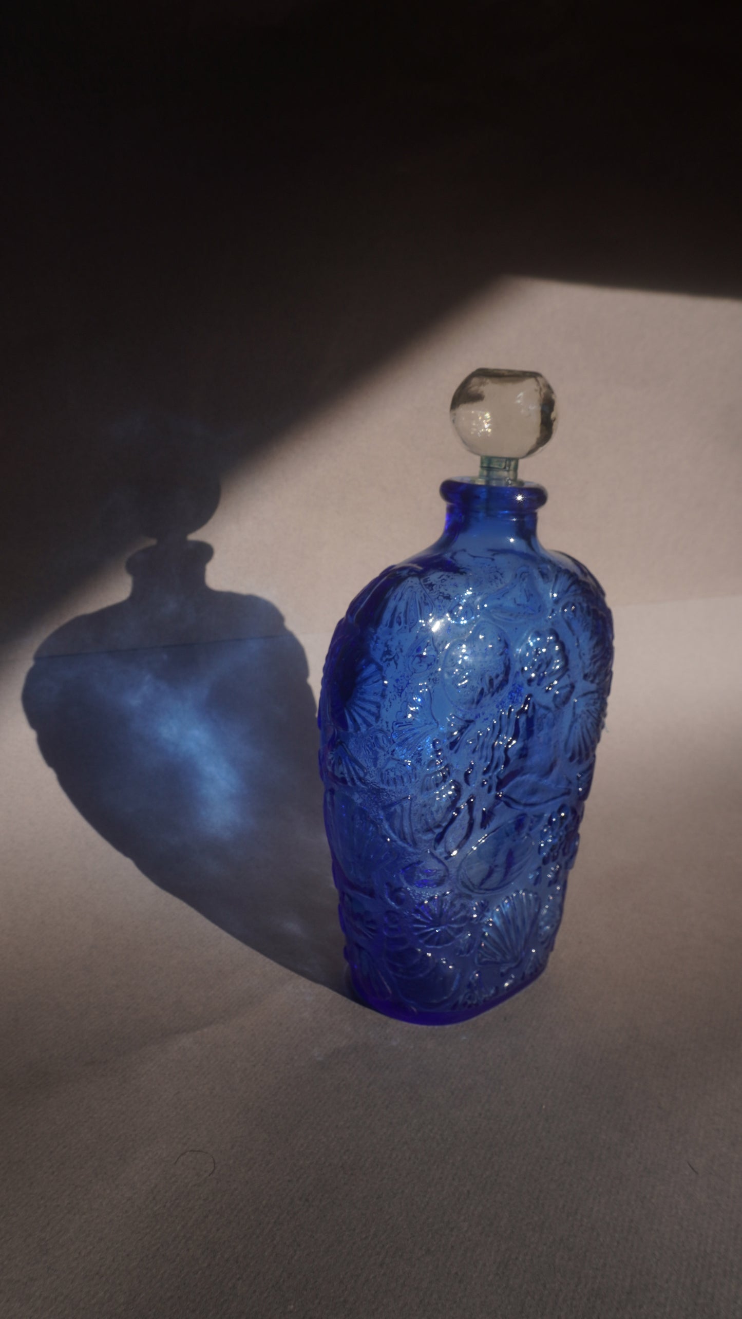 Blue glass decanter with intricate design on a gray background