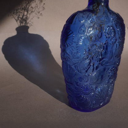 Blue glass decanter with intricate patterns on a plain background
