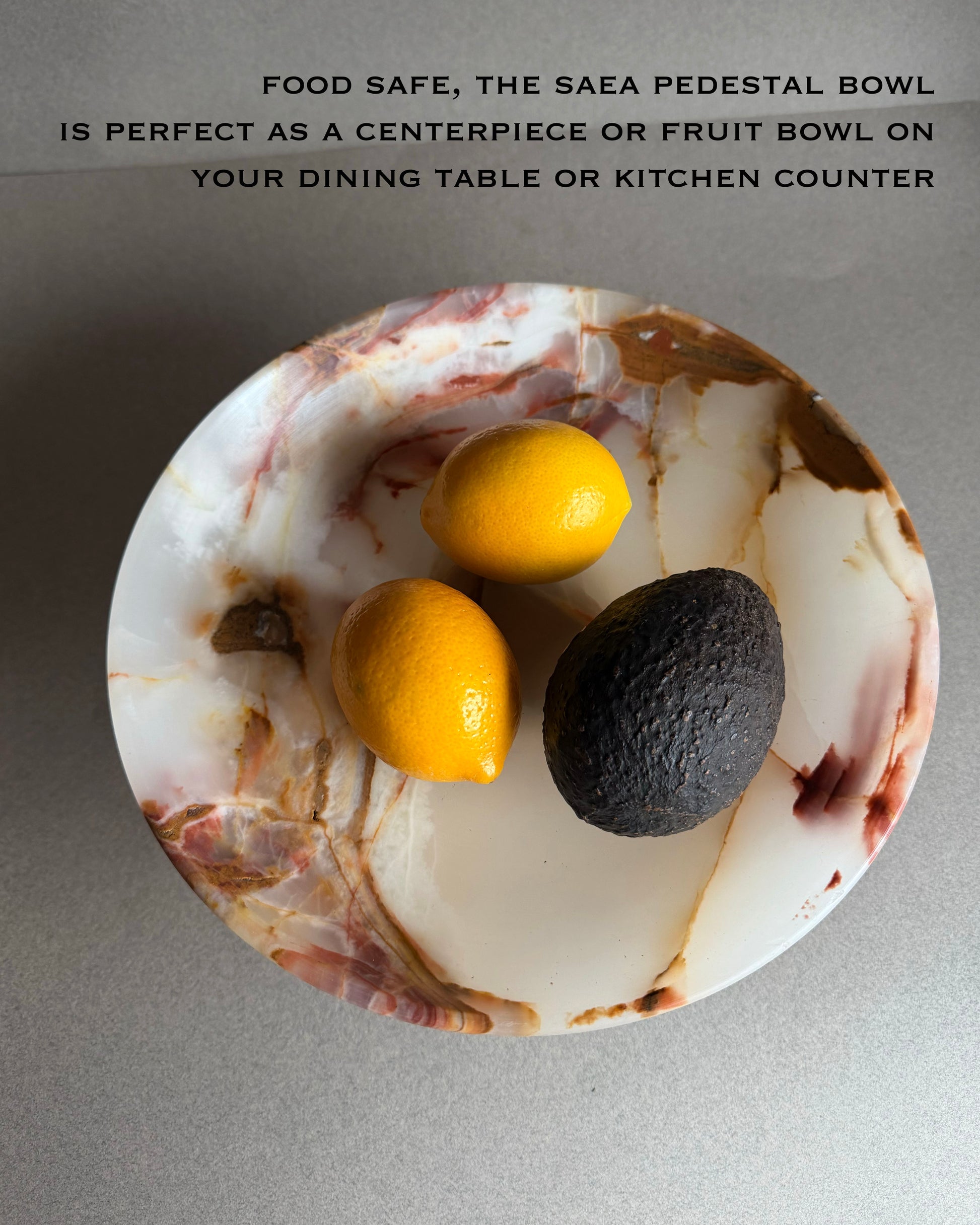 Marble pedestal bowl with lemons and an avocado on a gray background